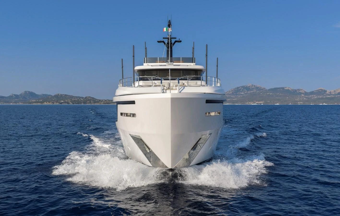 A sleek and modern yacht cruises forward on a calm sea with a stunning backdrop of distant mountains. aboard CLAIRE DE LUNE Yacht for Sale
