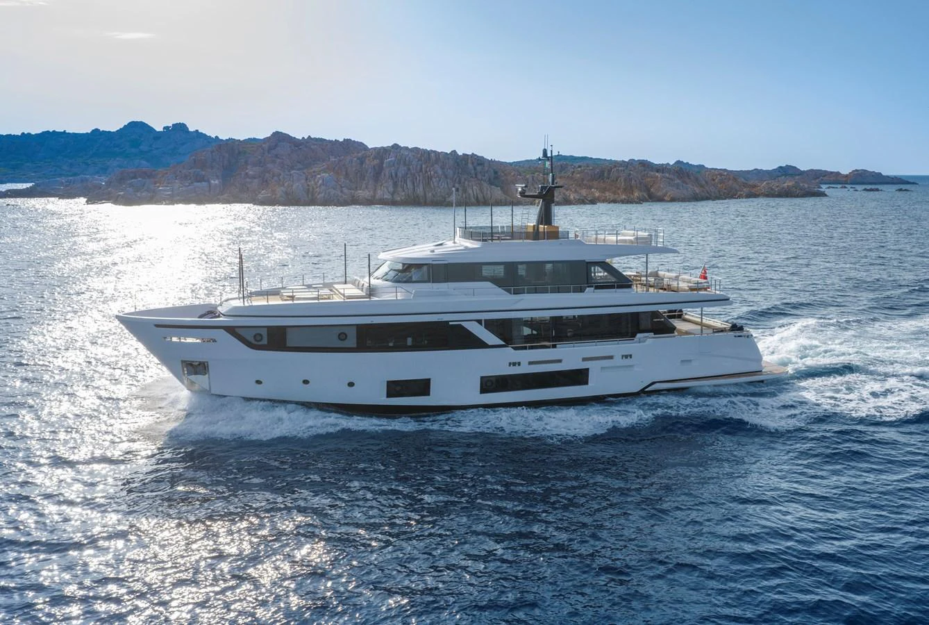 A sleek and modern yacht cruises through calm waters with a scenic rocky coastline in the background. aboard CLAIRE DE LUNE Yacht for Sale