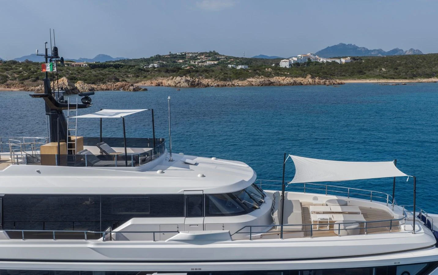 A sleek yacht is anchored near a picturesque coastline with clear blue waters and distant hills. aboard CLAIRE DE LUNE Yacht for Sale