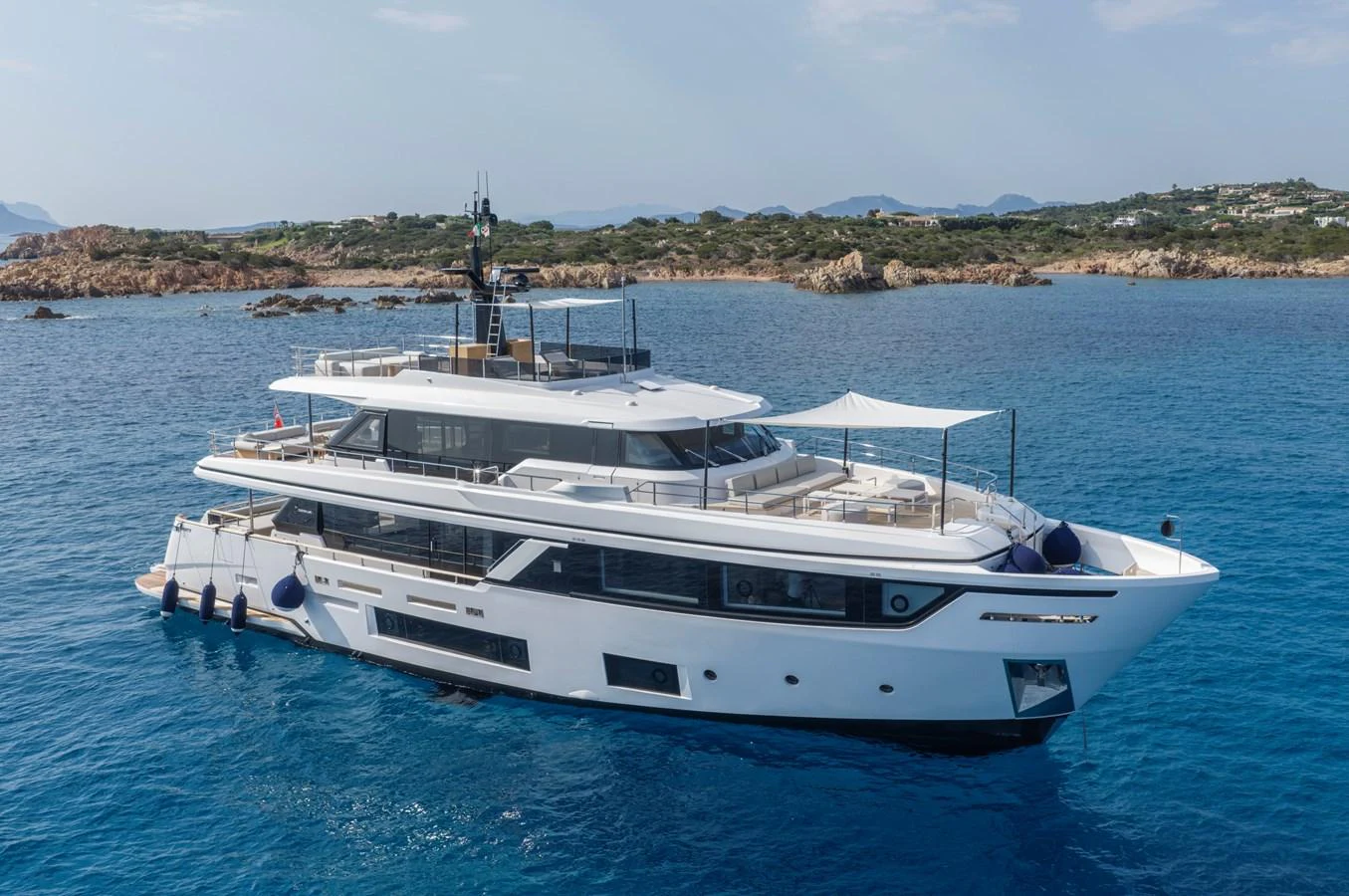 A luxurious yacht is anchored in serene blue waters with a scenic coastline in the background. aboard CLAIRE DE LUNE Yacht for Sale