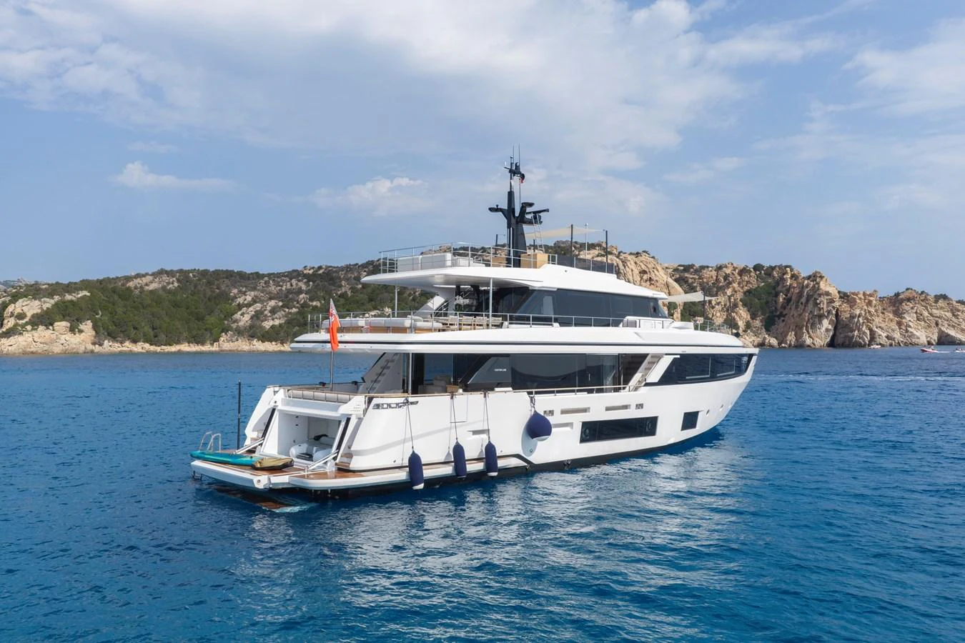 A sleek and modern yacht is anchored in a serene, blue-water bay with a rocky coastline in the background. aboard CLAIRE DE LUNE Yacht for Sale