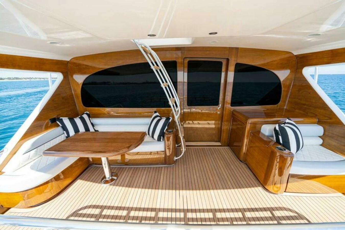 The aft deck features elegant wooden finishes, comfortable seating, and a dining table with a view of the sea. aboard 2027 VIKING 90SB Yacht for Sale