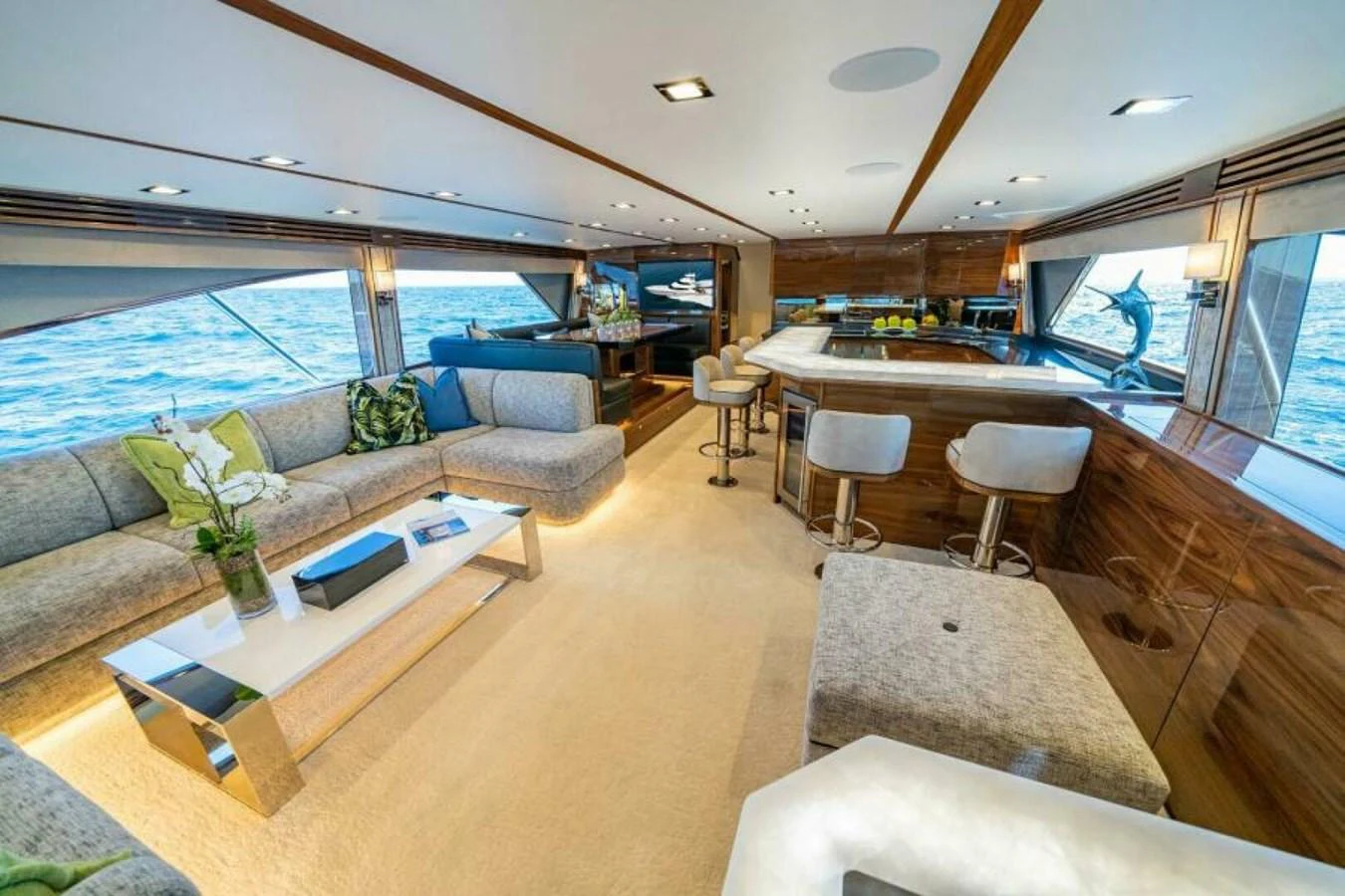 The salon features luxurious seating, a modern bar, and panoramic windows with ocean views. aboard 2027 VIKING 90SB Yacht for Sale