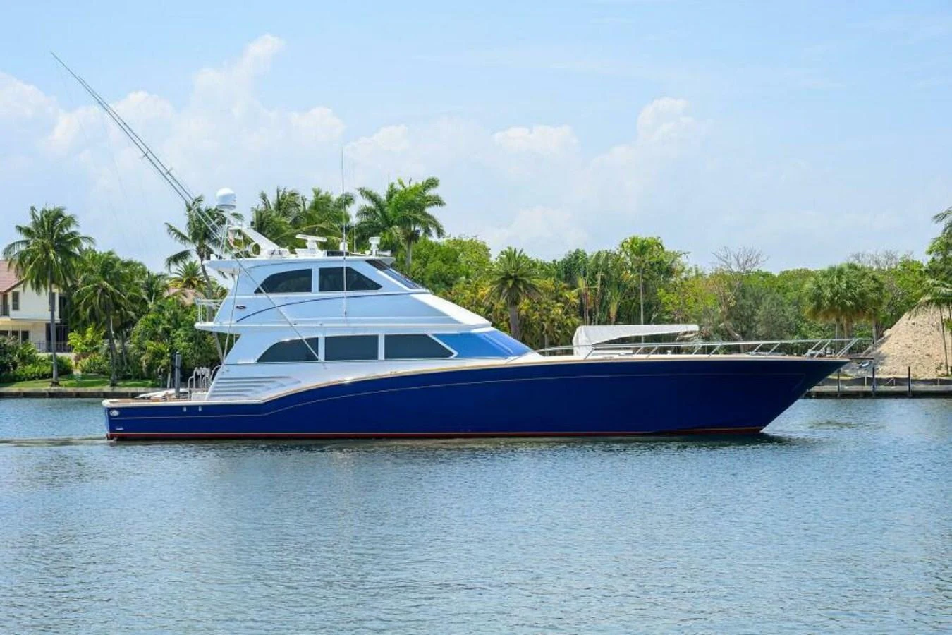 A sleek yacht with a striking blue hull cruising on calm waters near a tropical shoreline. aboard JUNIOR Yacht for Sale