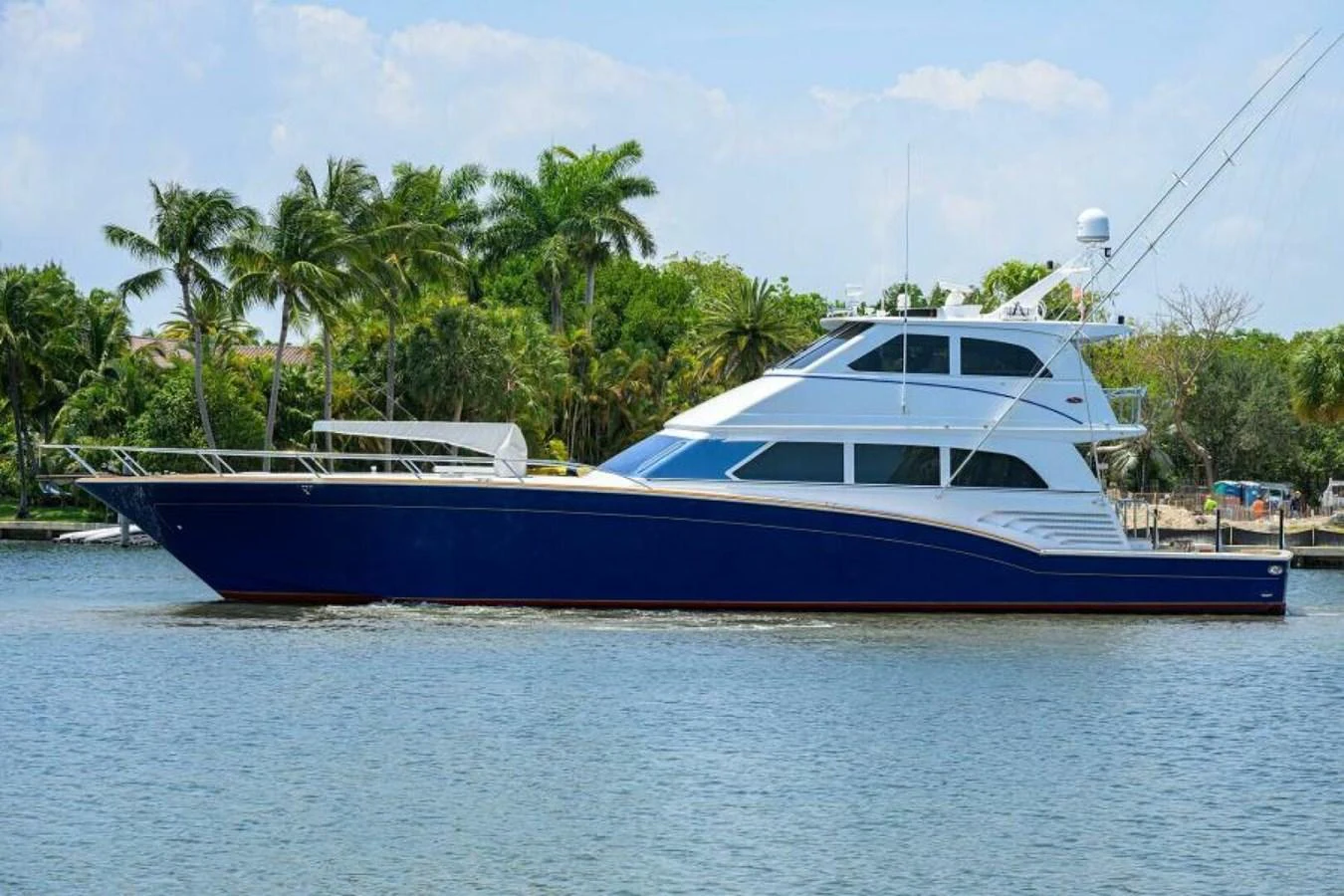 A sleek yacht with a deep blue hull is anchored near a lush, tropical shoreline. aboard JUNIOR Yacht for Sale