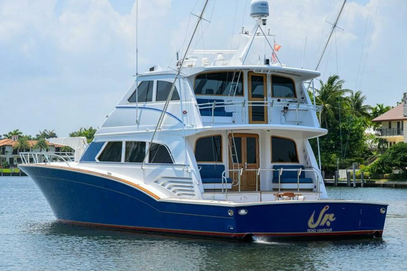 A luxurious yacht with a sleek blue hull cruising near waterfront homes. aboard JUNIOR Yacht for Sale