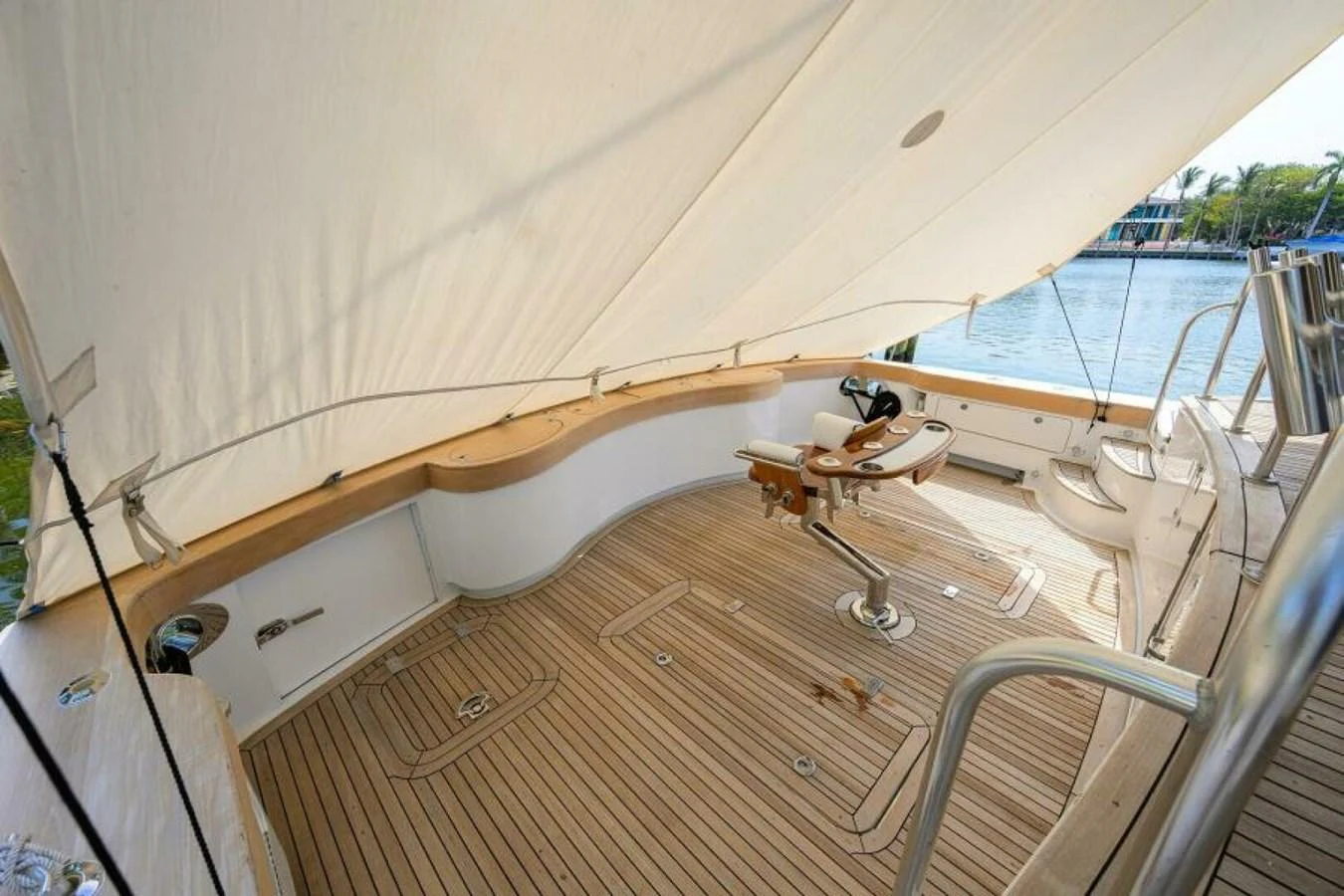 The aft deck features a shaded seating area with a wooden helm and a view of the water. aboard JUNIOR Yacht for Sale