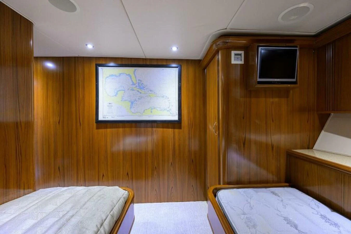 The stateroom features twin beds, wood paneling, and a wall-mounted map for a cozy and functional space. aboard JUNIOR Yacht for Sale