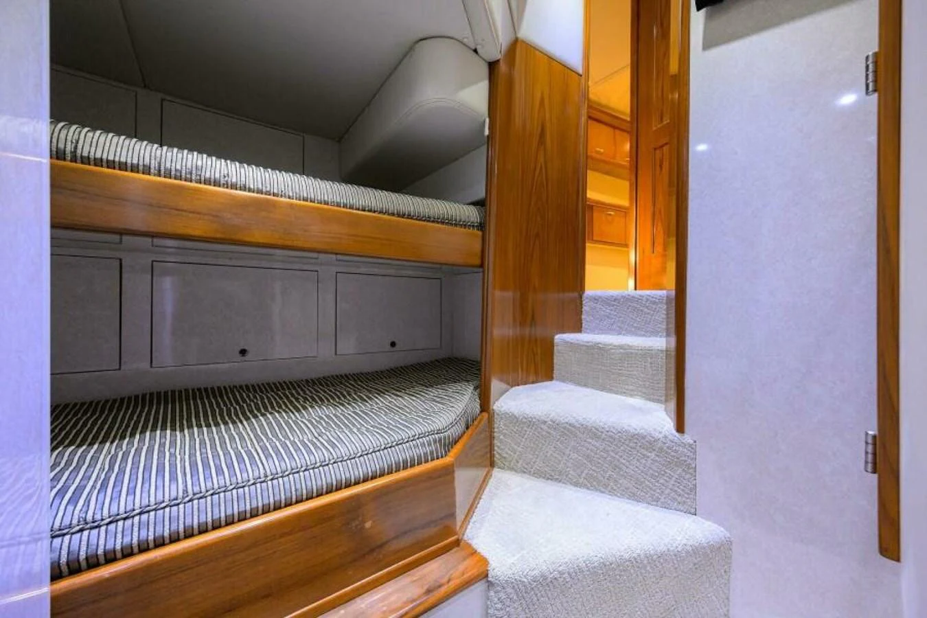 The cozy bunk room features wooden accents and comfortable striped bedding. aboard JUNIOR Yacht for Sale