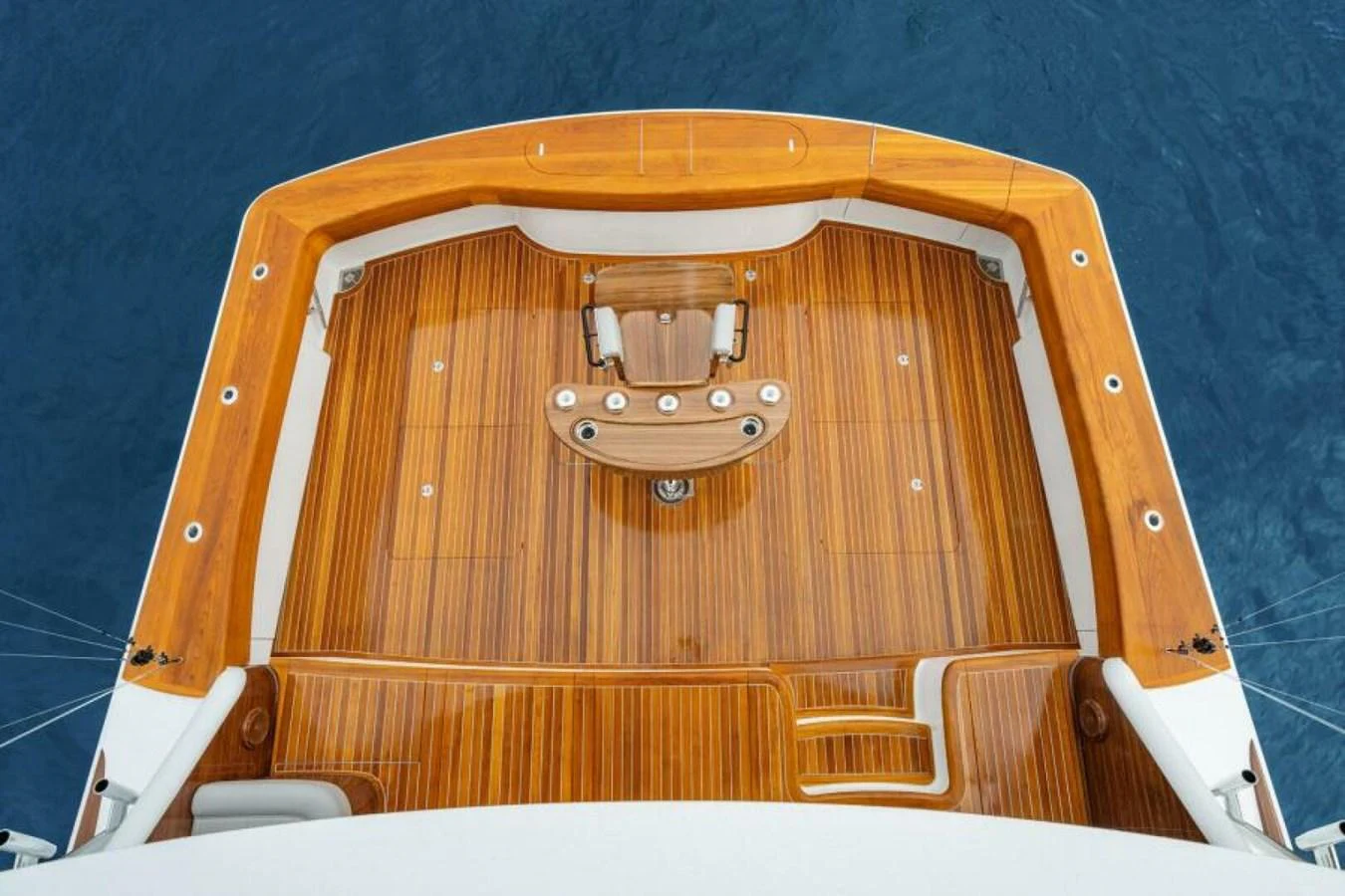 The yacht's aft deck features a beautifully finished teak floor with a central seating area, overlooking the serene blue water. aboard 2027 VIKING 82C Yacht for Sale