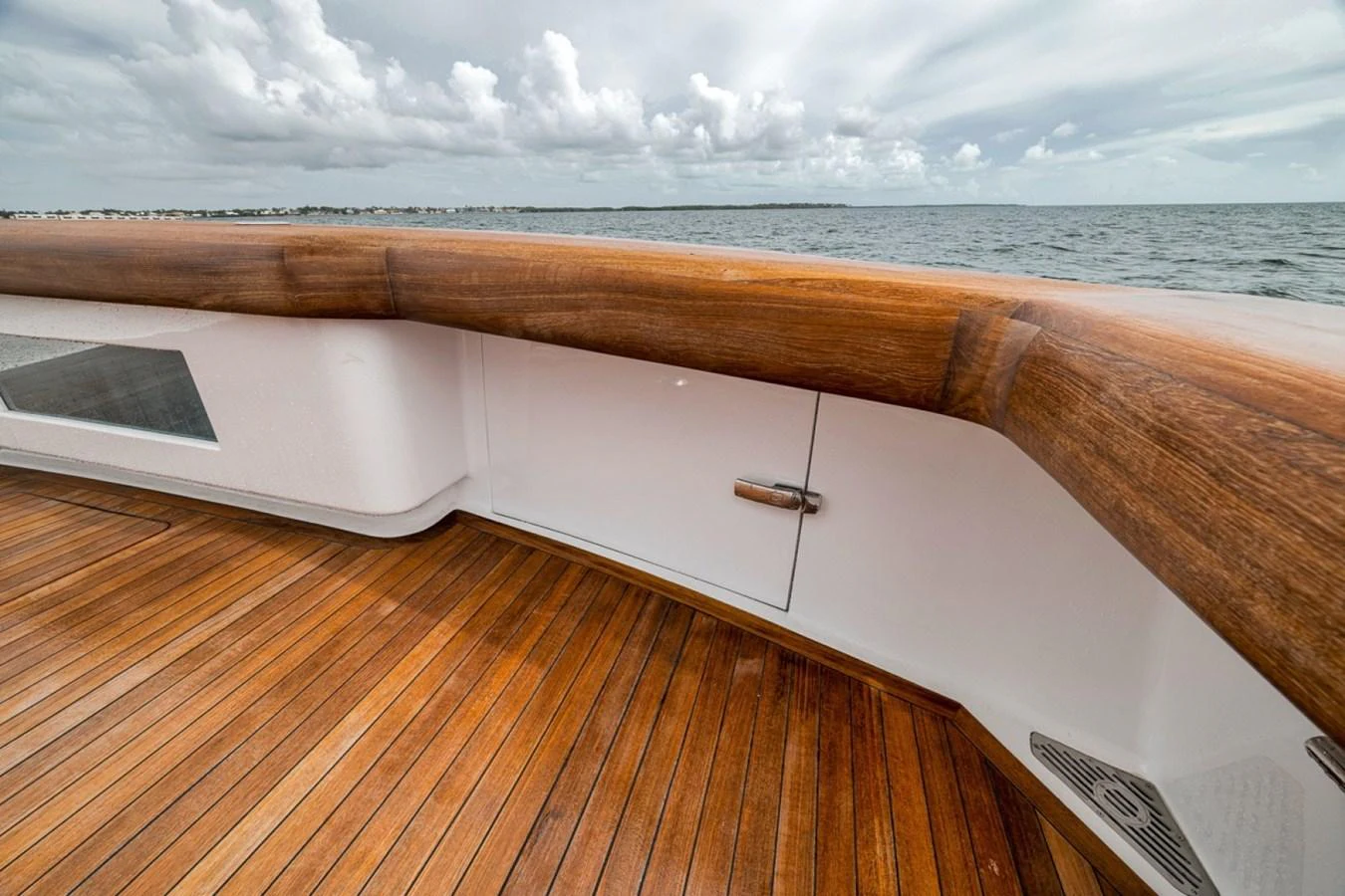 A close-up view of the yacht's teak deck and wooden railing, with the ocean in the background. aboard GENESIS Yacht for Sale