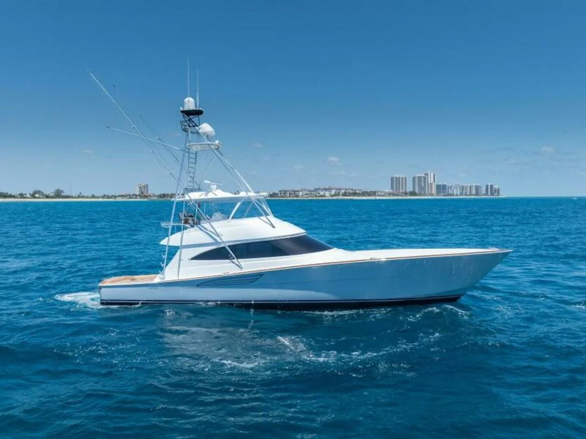 A sleek yacht cruises on a clear blue sea with a cityscape in the background. aboard 2027 VIKING 74C Yacht for Sale