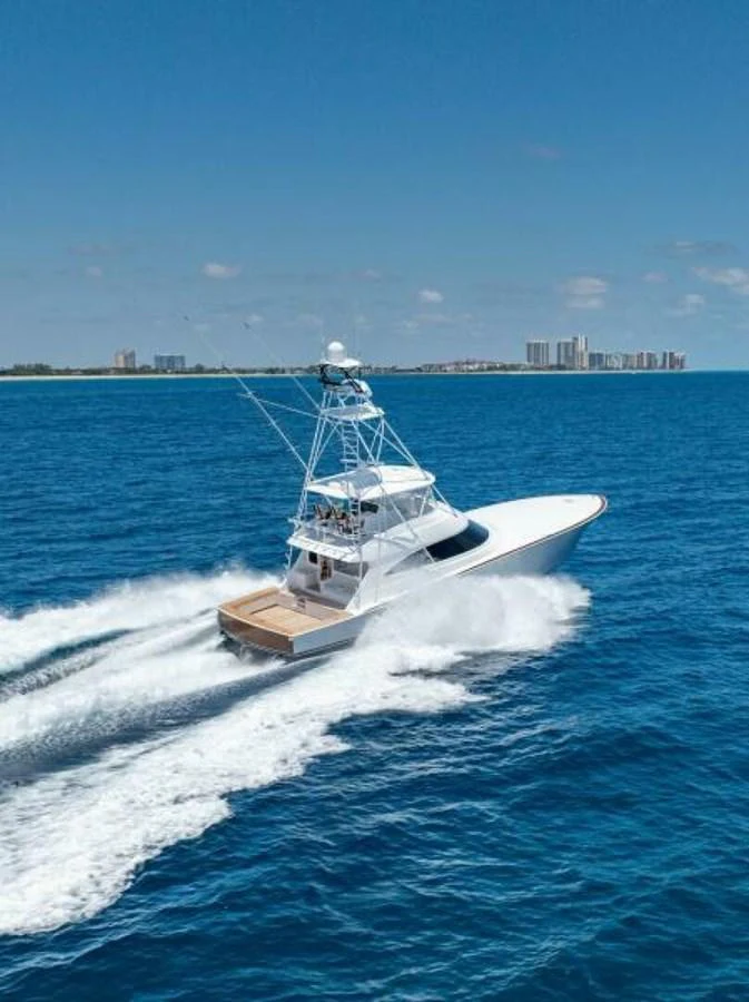 A sleek yacht cruises swiftly through the vibrant blue waters near a coastal city. aboard 2027 VIKING 74C Yacht for Sale