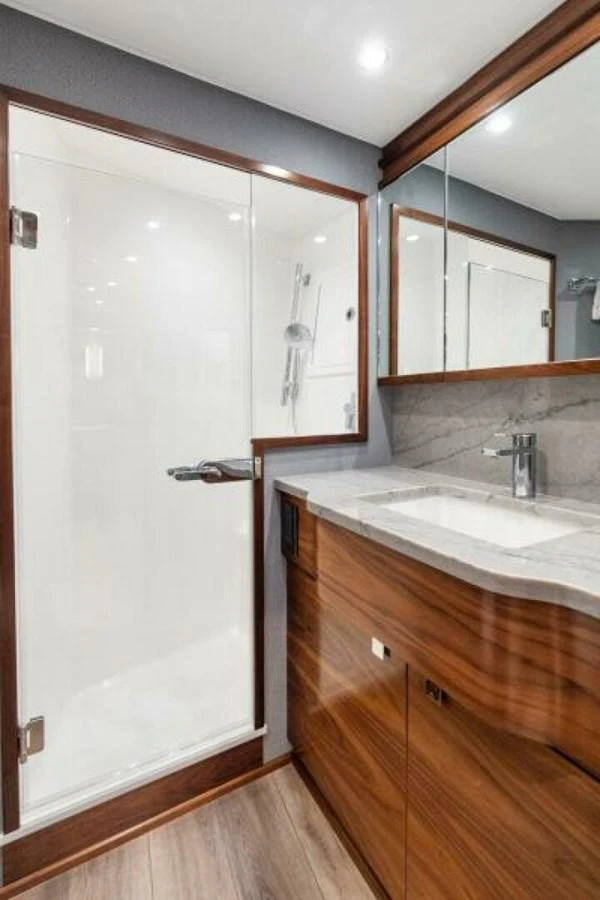 The yacht's bathroom features a sleek design with a glass-enclosed shower and a polished wooden vanity. aboard 2027 VIKING 74C Yacht for Sale