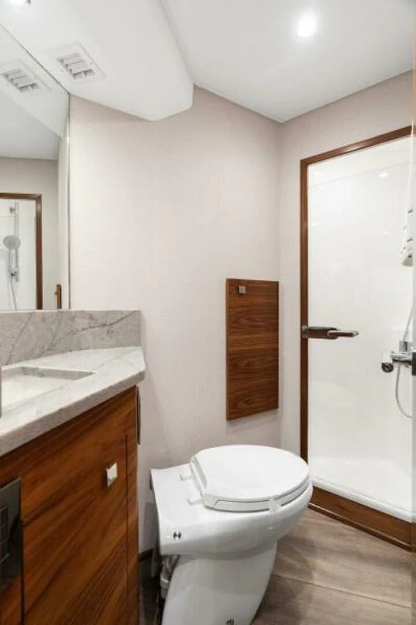 The yacht's head features a modern design with a sleek toilet, a marble countertop, and a glass-enclosed shower. aboard 2027 VIKING 74C Yacht for Sale