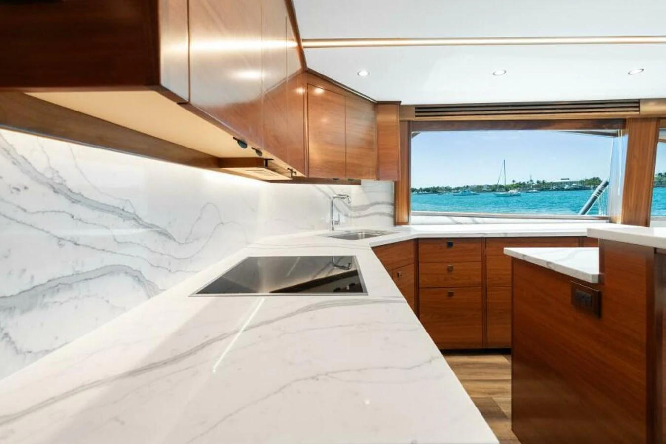 The galley features sleek marble countertops and rich wooden cabinetry with a view of the water. aboard 2027 VIKING 74C Yacht for Sale