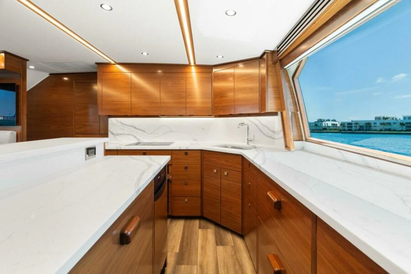 The yacht's galley features sleek wooden cabinetry and expansive marble countertops with a stunning view through large windows. aboard 2027 VIKING 74C Yacht for Sale