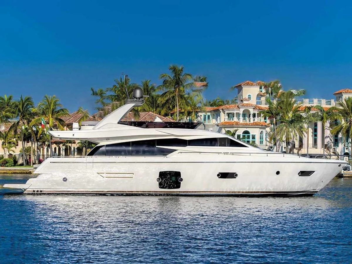 A sleek and modern yacht cruises along a picturesque waterfront with luxurious residences in the background. aboard LA LUNA Yacht for Sale