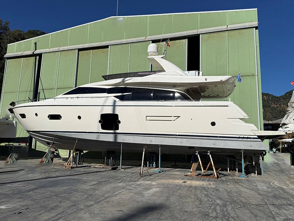 A sleek yacht is positioned on land, showcasing its elegant profile against a green industrial backdrop. aboard LA LUNA Yacht for Sale