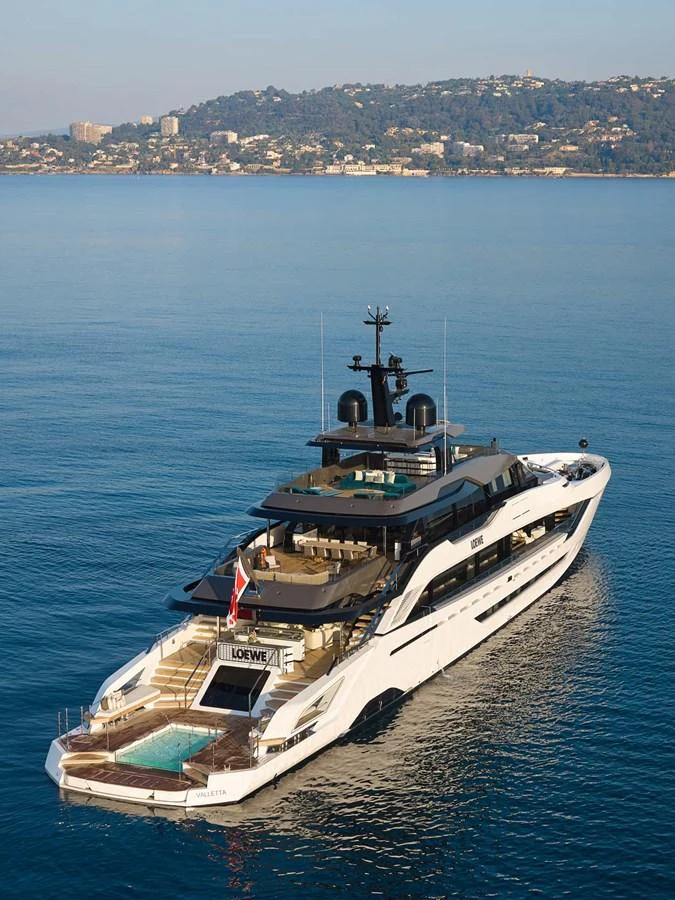 A luxurious yacht cruises on calm waters with a scenic coastal backdrop. aboard LOEWE Yacht for Sale