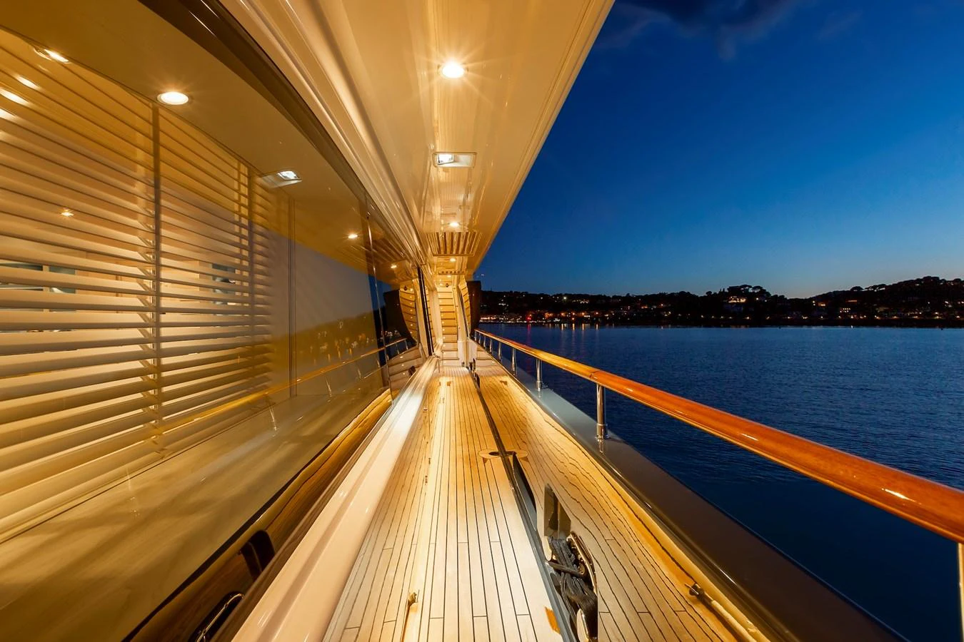 The yacht's side deck is beautifully illuminated, offering a serene view of the water at dusk. aboard LADY TRUDY Yacht for Sale