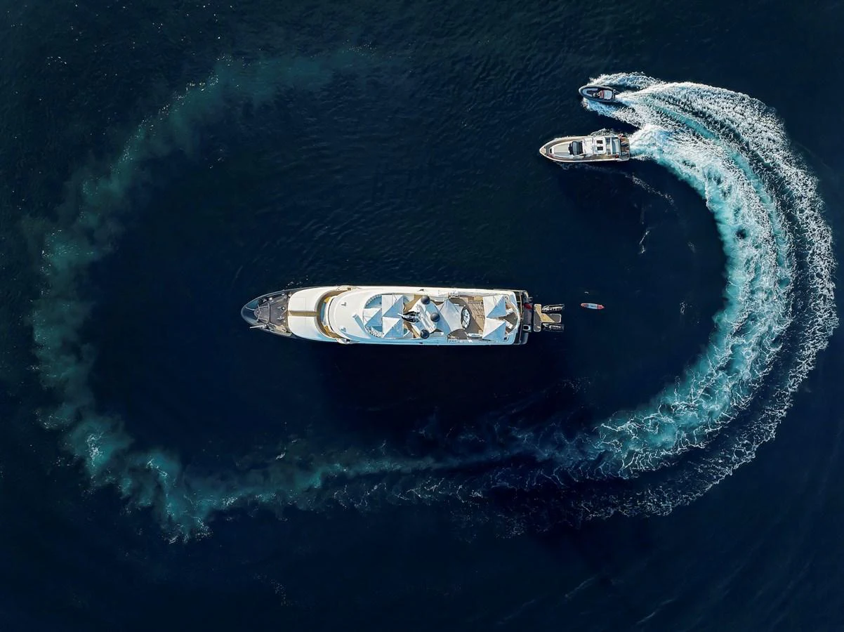 An aerial view of a yacht cruising through the water with a smaller boat creating a dynamic wake pattern. aboard LADY TRUDY Yacht for Sale