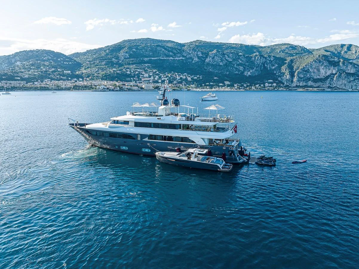 A luxurious yacht anchored in a scenic bay with tenders alongside. aboard LADY TRUDY Yacht for Sale