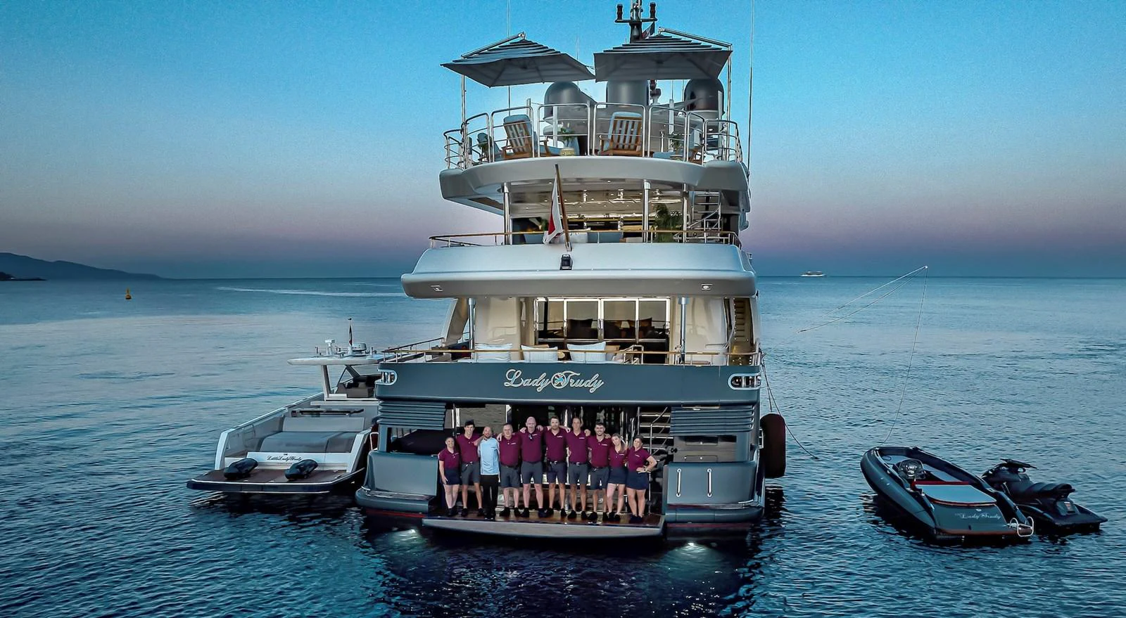 The crew poses on the aft deck of the yacht at sunset, showcasing the vessel's spacious and inviting rear area. aboard LADY TRUDY Yacht for Sale