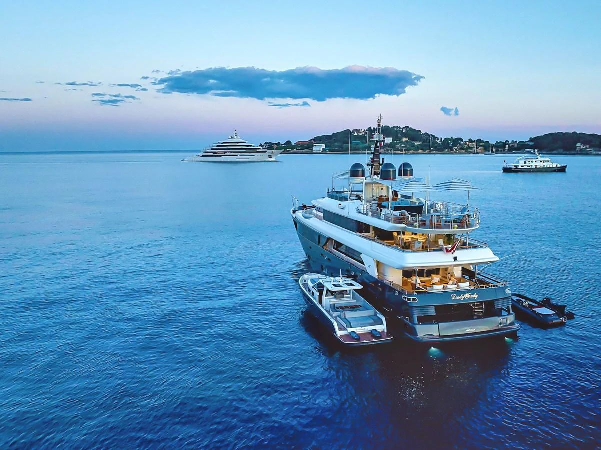 A luxurious yacht anchored in calm waters during sunset, accompanied by smaller boats. aboard LADY TRUDY Yacht for Sale