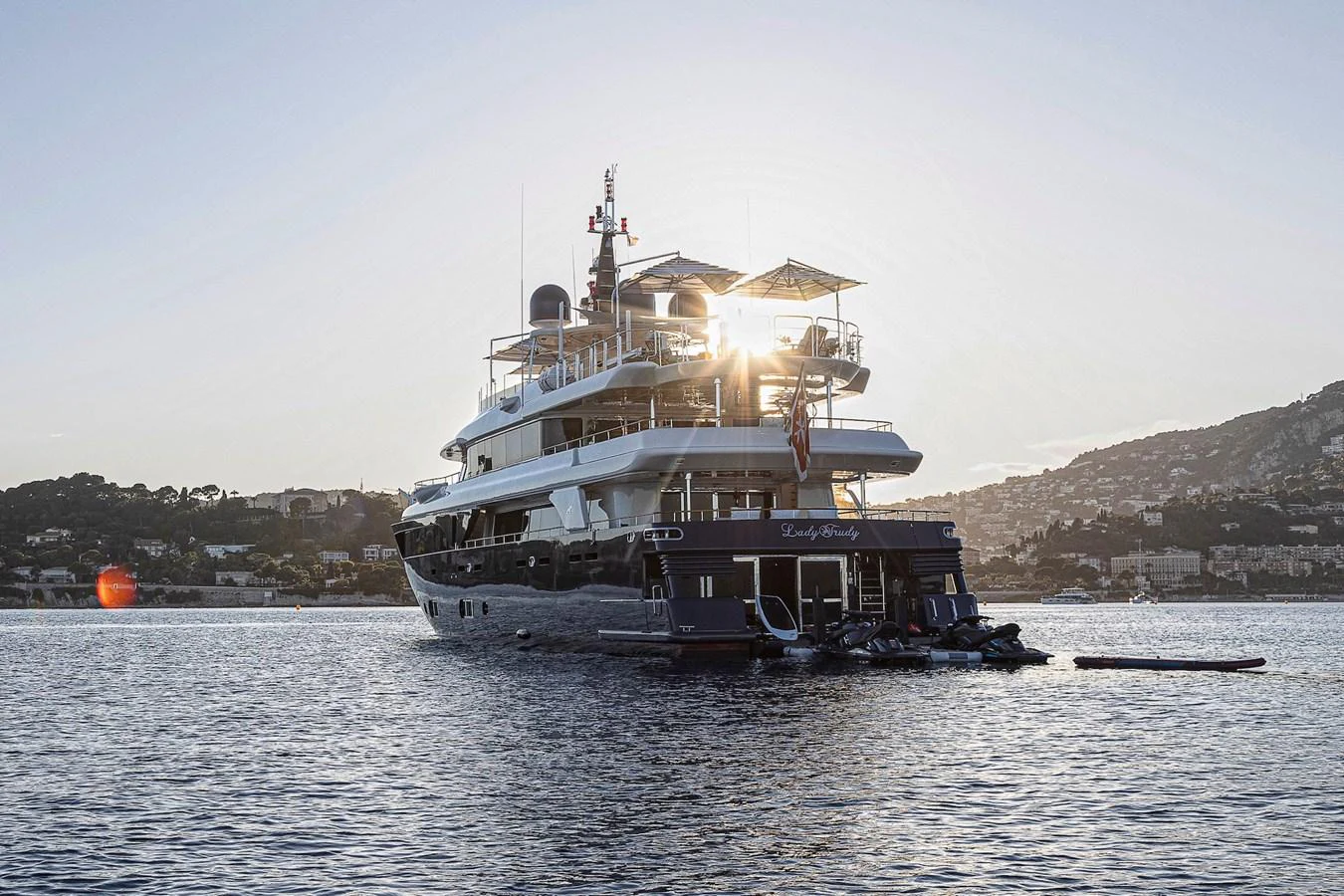 A luxurious yacht is anchored in calm waters with a scenic backdrop of hills and buildings. aboard LADY TRUDY Yacht for Sale