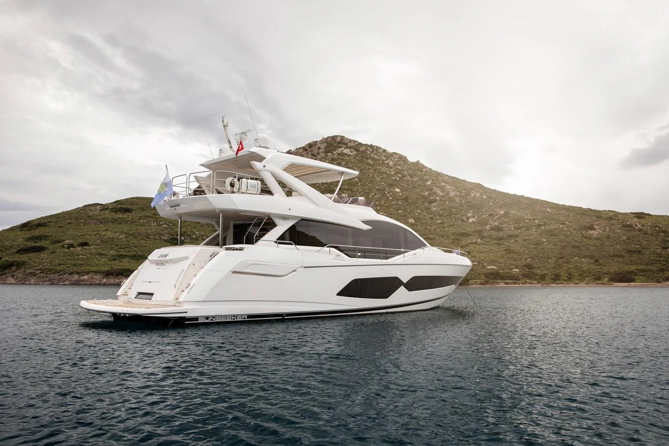 A sleek and modern yacht is anchored in calm waters with a scenic backdrop of hills. aboard ANM Yacht for Sale