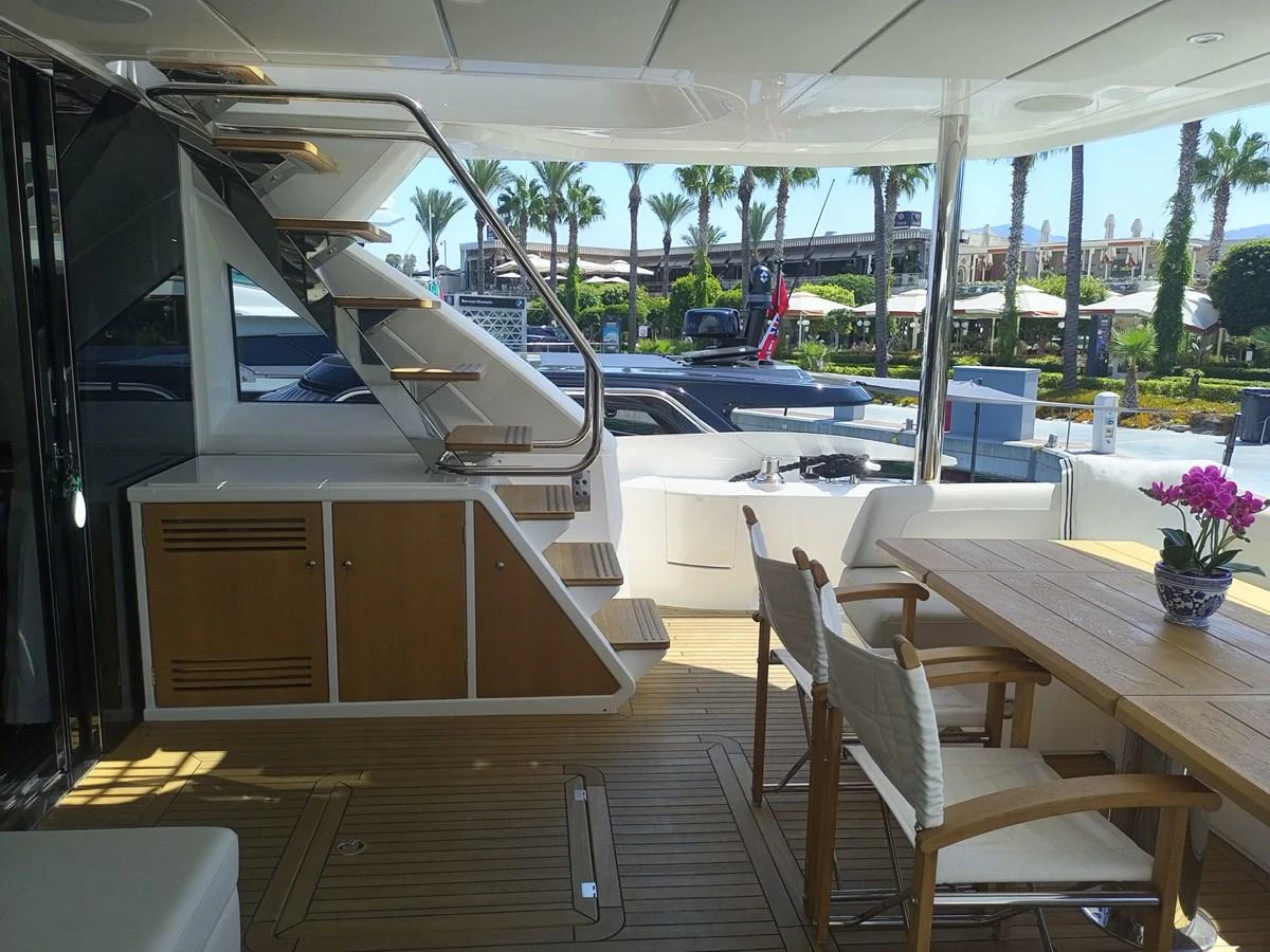 The aft deck features a comfortable dining area with a wooden table and chairs, complemented by a staircase leading to the upper deck. aboard ANM Yacht for Sale