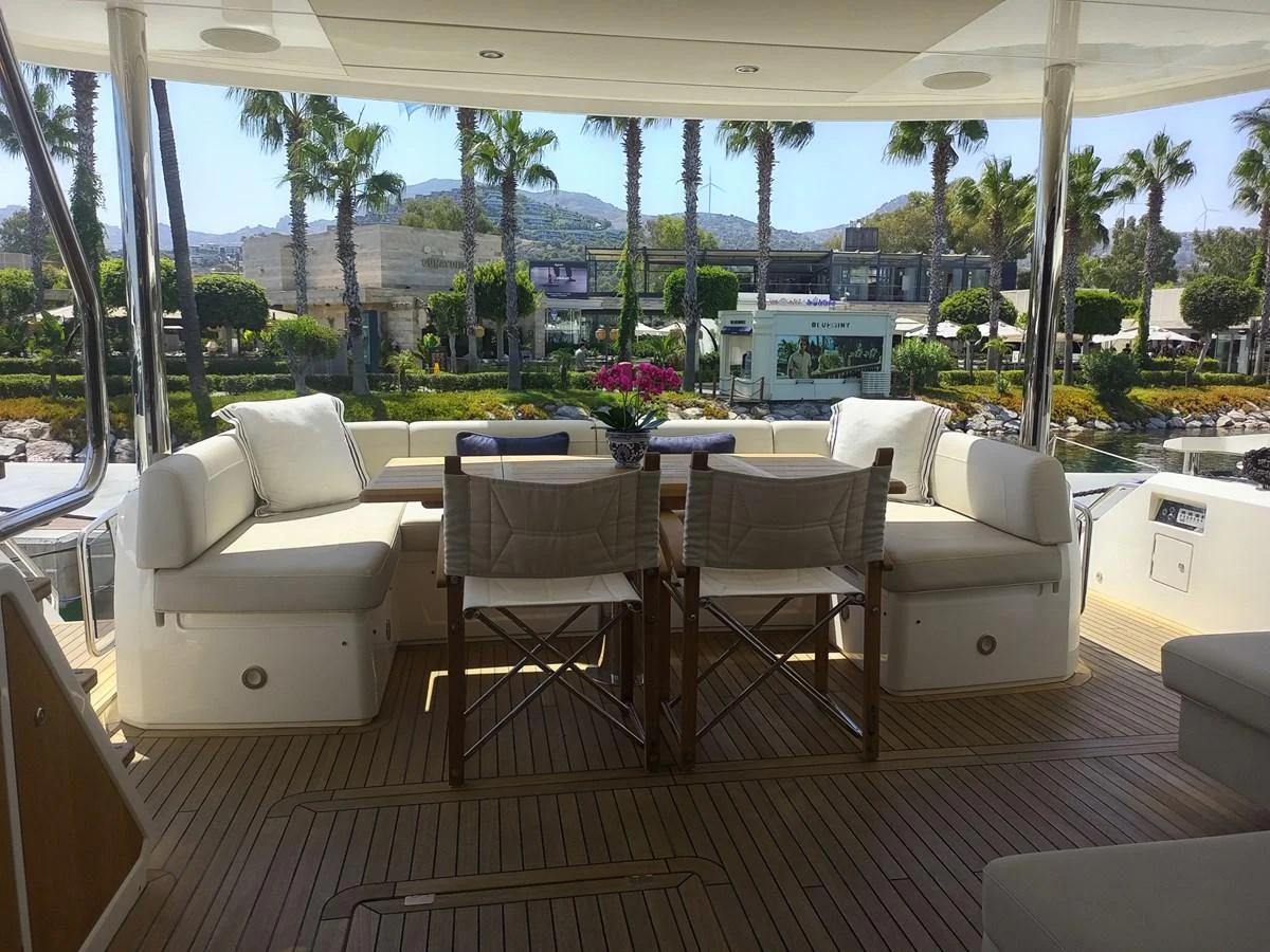 The aft deck offers a comfortable seating area with a scenic view of palm trees and a marina. aboard ANM Yacht for Sale
