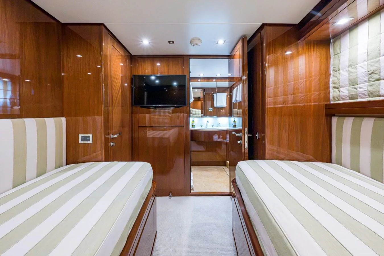 The twin stateroom features two comfortable beds with striped bedding and a view into the ensuite bathroom. aboard ALEGHI Yacht for Sale