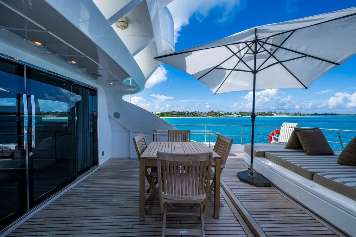 The aft deck features a stylish outdoor dining area with a wooden table and chairs, complemented by a large umbrella and sun loungers. aboard ALEGHI Yacht for Sale