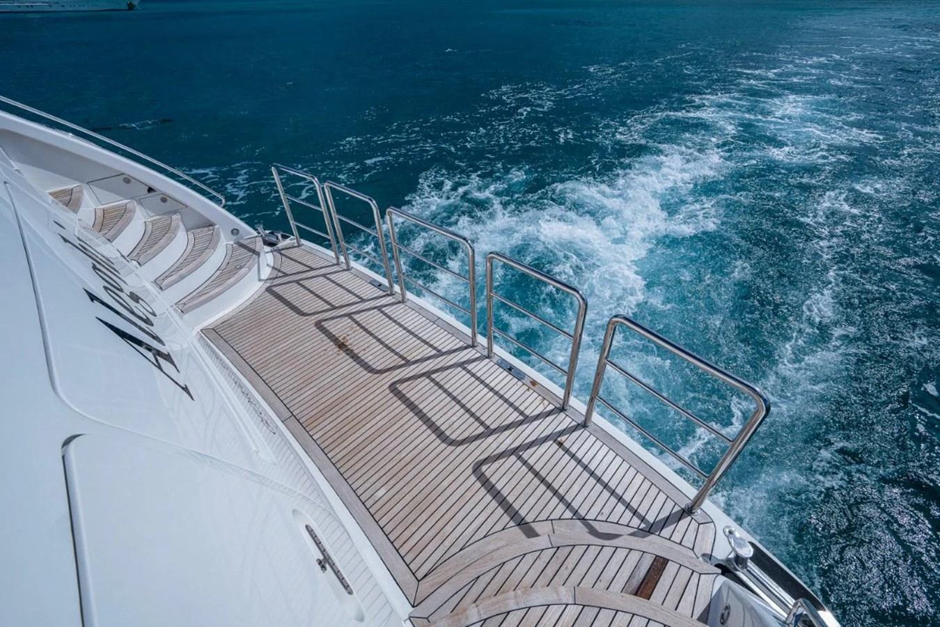 The aft deck of the yacht features elegant teak flooring and stainless steel railings, with a view of the wake trailing behind. aboard ALEGHI Yacht for Sale