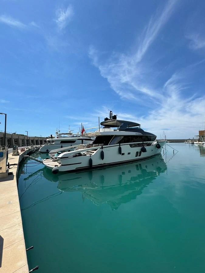 A sleek yacht is docked in a serene marina under a clear blue sky. aboard BELLA B Yacht for Sale