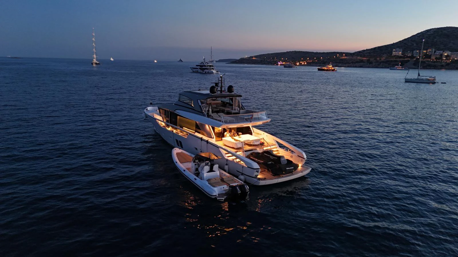 A luxurious yacht is anchored at dusk, illuminated warmly against the serene backdrop of the sea. aboard BELLA B Yacht for Sale