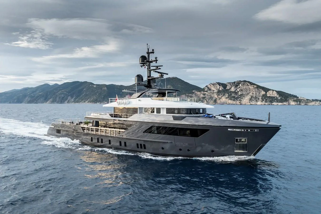 A sleek, modern yacht cruises through open waters with scenic mountains in the background. aboard BIG SHARK Yacht for Sale