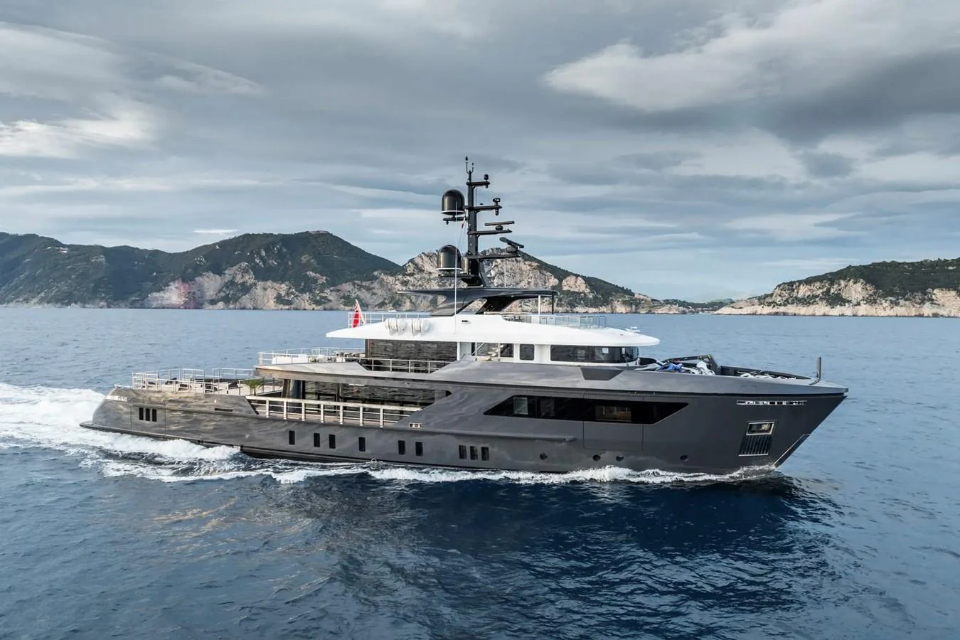 A sleek and modern yacht cruises through calm waters against a backdrop of scenic mountains. aboard BIG SHARK Yacht for Sale