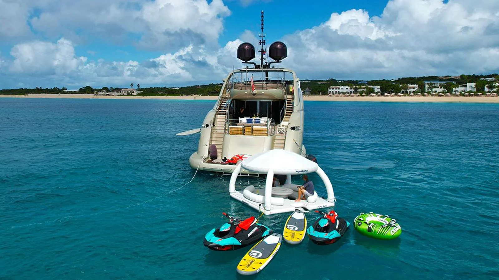 The yacht is anchored in clear blue waters with various water toys and inflatables nearby. aboard YCM 120 Yacht for Sale