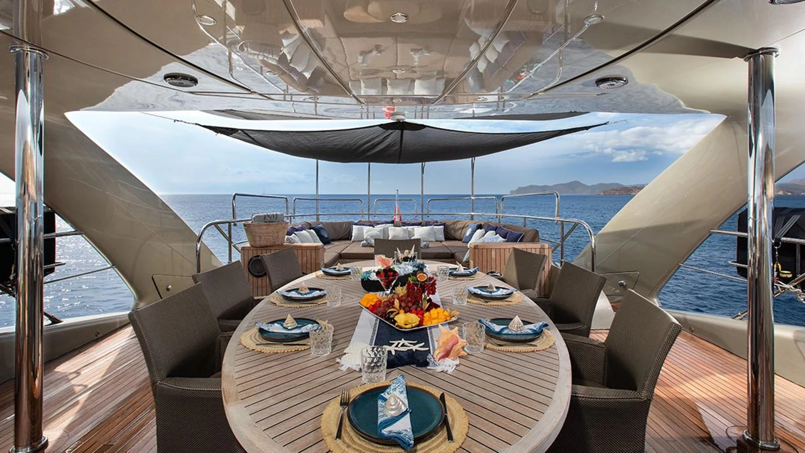 The aft deck features an elegant dining area with a round table set for a meal, offering stunning ocean views. aboard YCM 120 Yacht for Sale