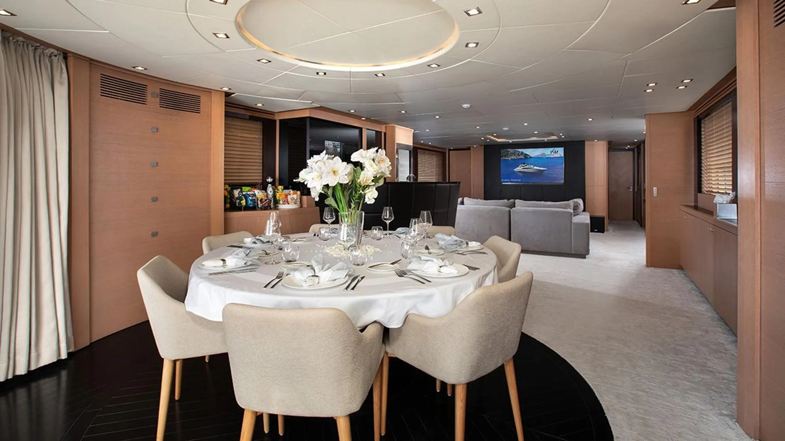 The yacht's dining area features a stylish table set for a meal, with a comfortable lounge area in the background. aboard YCM 120 Yacht for Sale