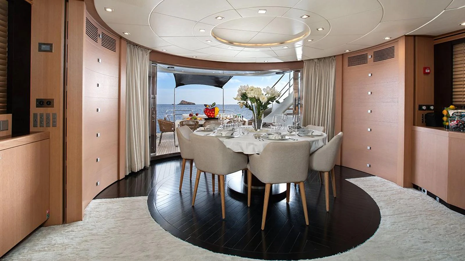 The elegant dining area features a round table set for a meal, with a view of the sea through large windows. aboard YCM 120 Yacht for Sale