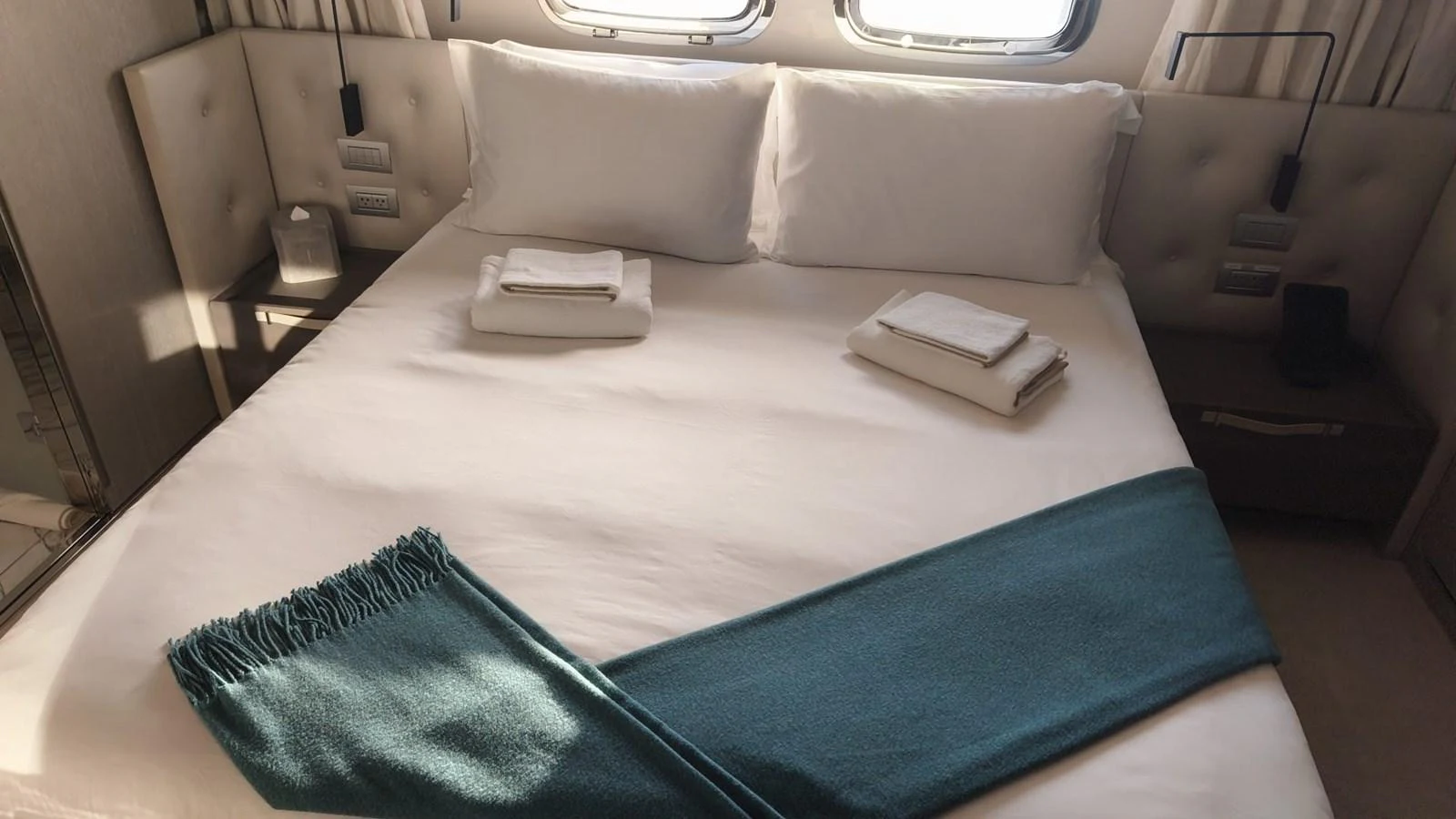 A cozy stateroom features a neatly made bed with plush pillows and a teal throw blanket. aboard HONEY Yacht for Sale