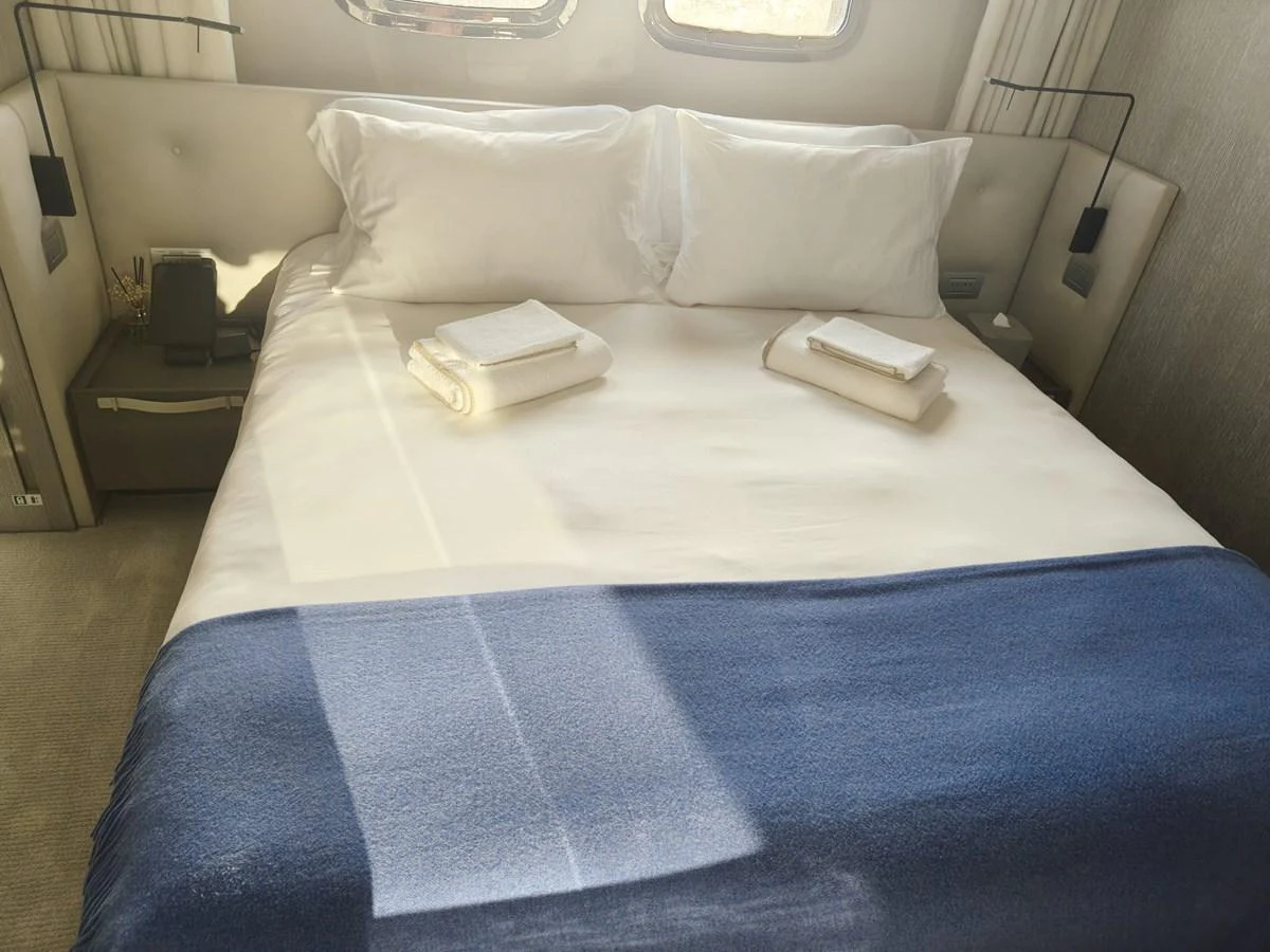 The stateroom features a plush bed with crisp linens and a cozy blanket, bathed in natural light. aboard HONEY Yacht for Sale