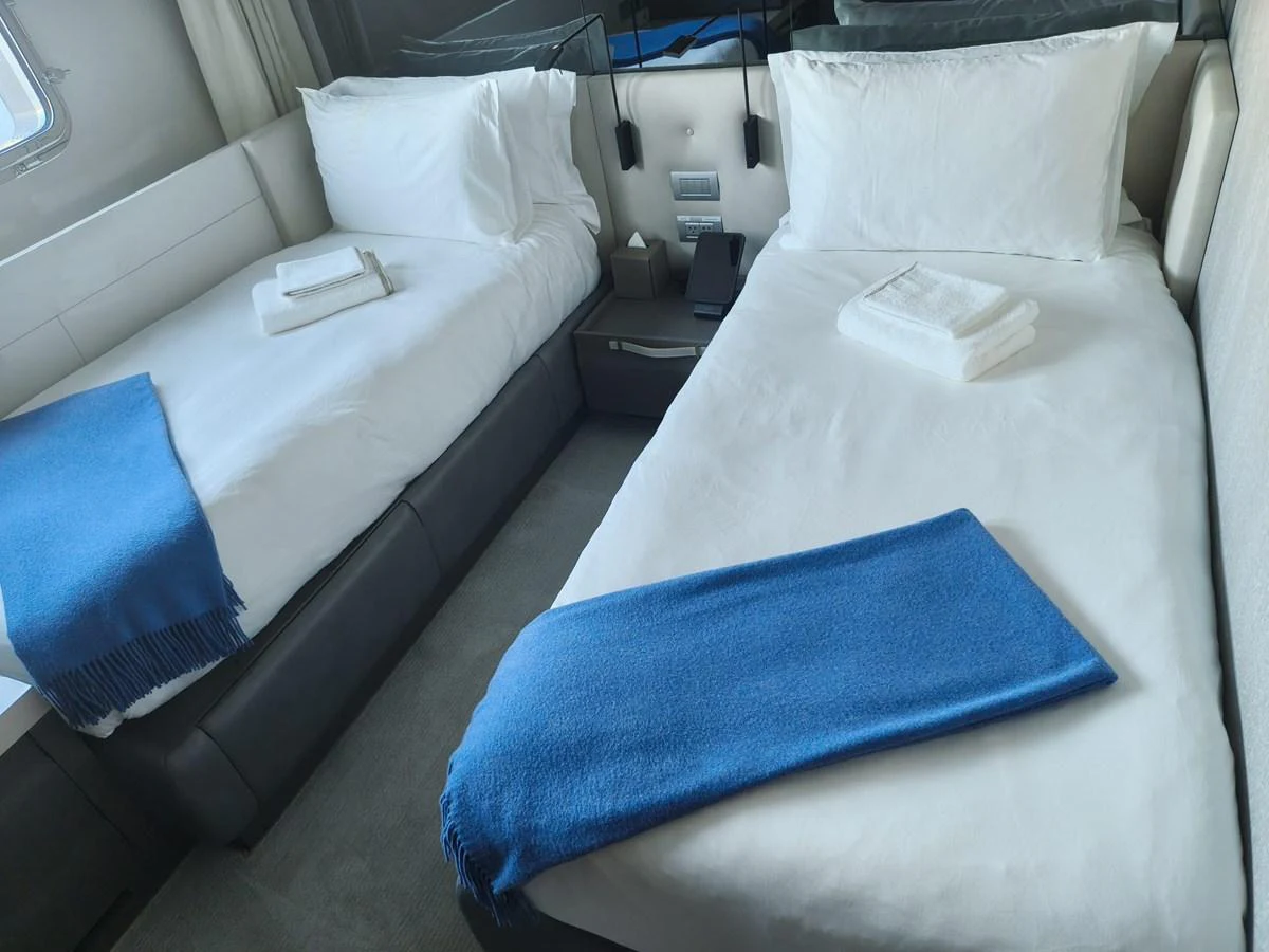 The twin stateroom features two comfortable beds with crisp white linens and blue accents. aboard HONEY Yacht for Sale