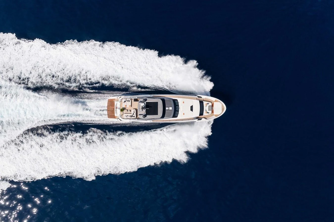 An aerial view of a sleek yacht cruising through deep blue waters, leaving a trail of white wake behind. aboard JACKI 8 Yacht for Sale