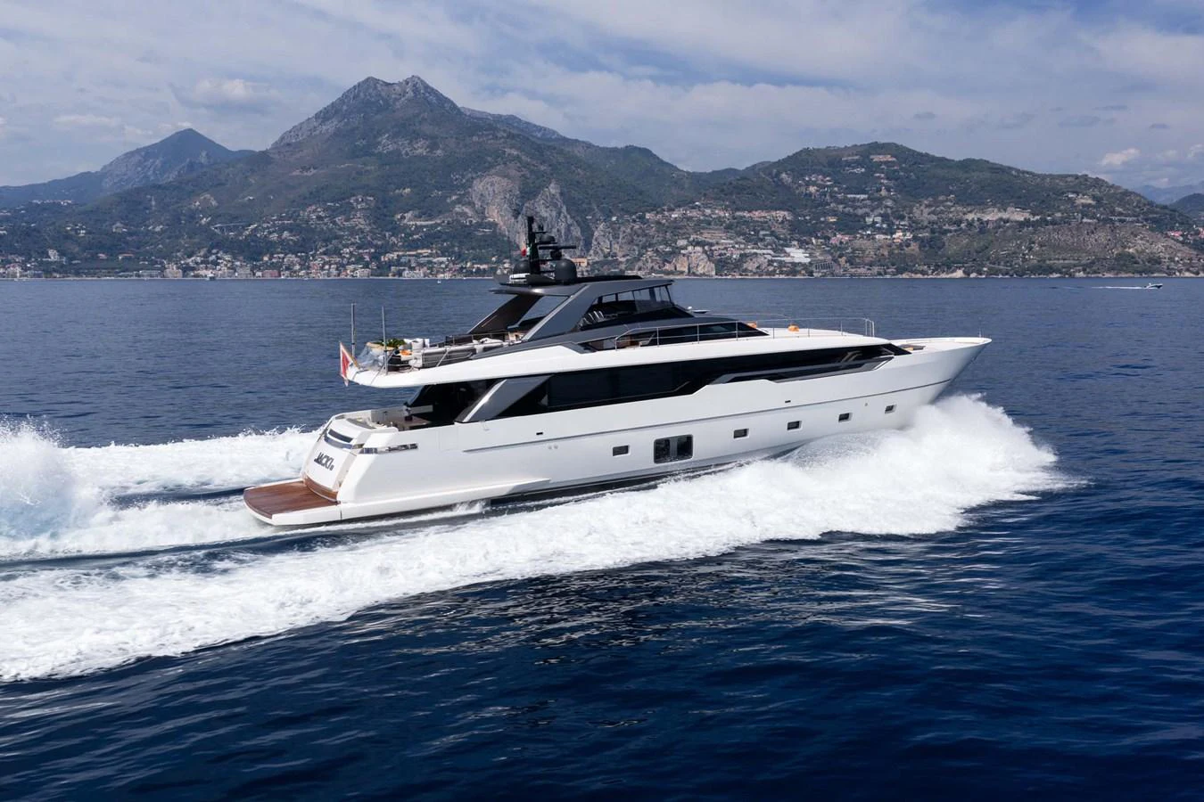 A sleek, modern yacht cruises through calm waters with a mountainous backdrop. aboard JACKI 8 Yacht for Sale