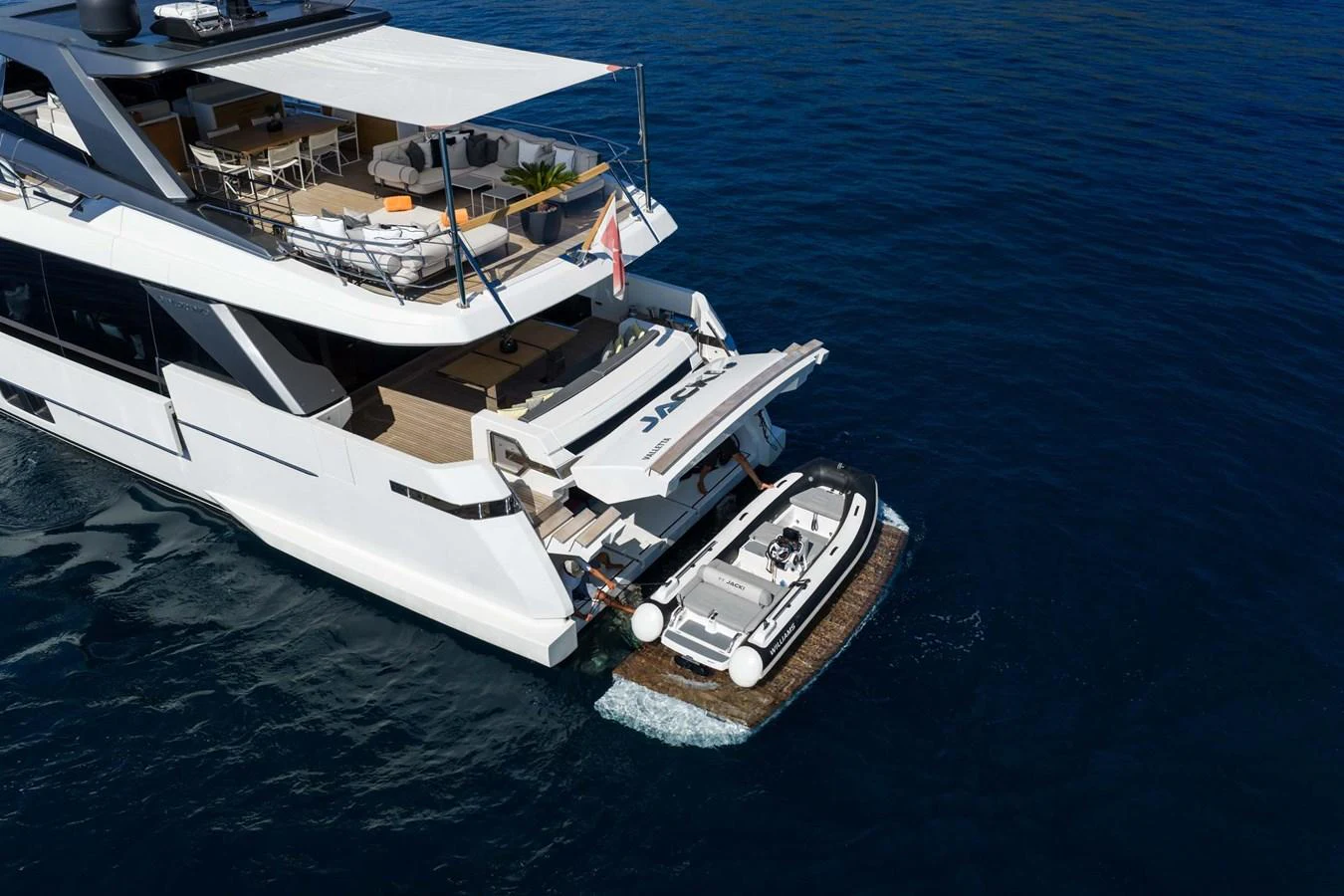 The yacht's aft deck features a spacious lounging area and a tender platform with a small boat. aboard JACKI 8 Yacht for Sale